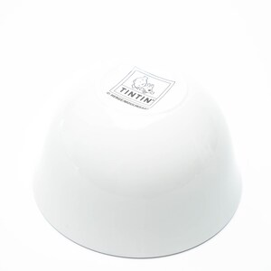 May include: White ceramic bowl with a rounded shape. The bowl features a logo with the word "TINTIN" and a cartoon image. The bowl is glossy and appears to be new.