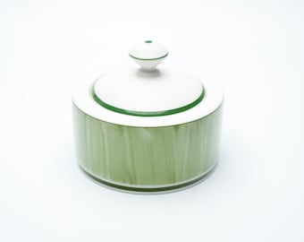 May include: A white and green ceramic sugar bowl with a lid. The cylindrical body is light green with vertical brushstrokes. The lid and finial are white with green trim. The sugar bowl is a kitchenware item.