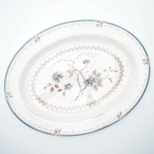 May include: An oval serving platter with a floral design. The off-white ceramic platter features a blue rim and a central floral motif in shades of blue and brown. Decorative elements include a dotted border and floral accents.
