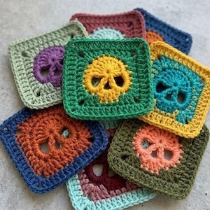 May include: A collection of colorful, square crochet patches, each featuring a skull design. The patches are in various colors, including green, orange, blue, and yellow, with the skull in a contrasting color. The crochet work is detailed and textured.
