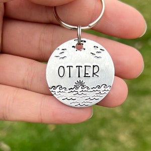 May include: Silver key chain with a round tag that says "OTTER" and has a design of waves and birds.