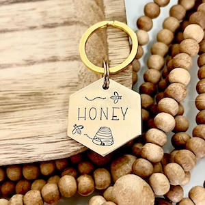 May include: Gold key chain with a hexagonal tag that says "Honey" with a beehive and bees engraved on it.