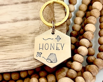 May include: Gold key chain with a hexagonal tag that says "Honey" with a beehive and bees engraved on it.