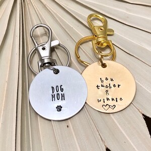 May include: Two silver keychains with round metal tags. One tag says "Dog Mom" with a paw print. The other tag is gold and says "Ben Tucker & Winnie" with two hearts.