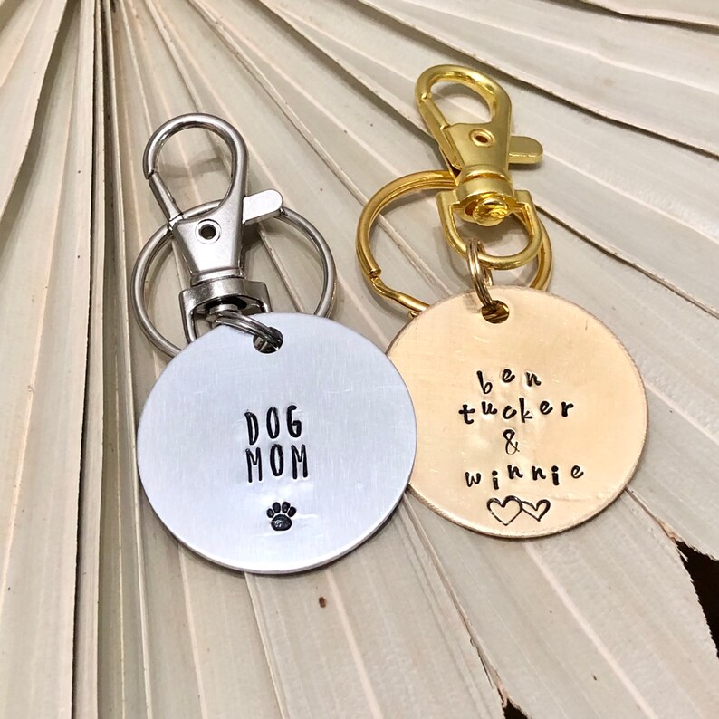 May include: Two silver keychains with round metal tags. One tag says "Dog Mom" with a paw print. The other tag is gold and says "Ben Tucker & Winnie" with two hearts.