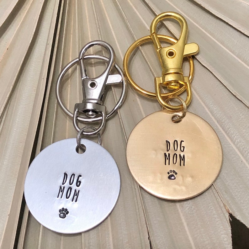 May include: Two silver and gold keychains with a round tag that says "Dog Mom" with a paw print.