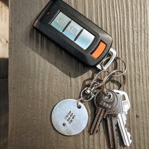 May include: A silver key chain with a round metal tag that says "Dog Mom" and a paw print. The keychain also has a black car key fob and three silver keys.
