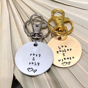 May include: Two silver and gold keychains with round metal tags. The silver tag says "Roxy & Ruby" with two small hearts. The gold tag says "Ben Tucker & Winnie" with two small hearts.