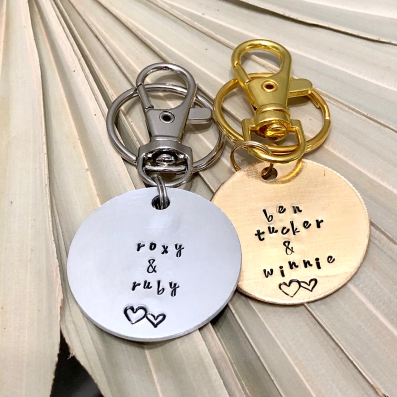 May include: Two silver and gold keychains with round metal tags. The silver tag says "Roxy & Ruby" with two small hearts. The gold tag says "Ben Tucker & Winnie" with two small hearts.