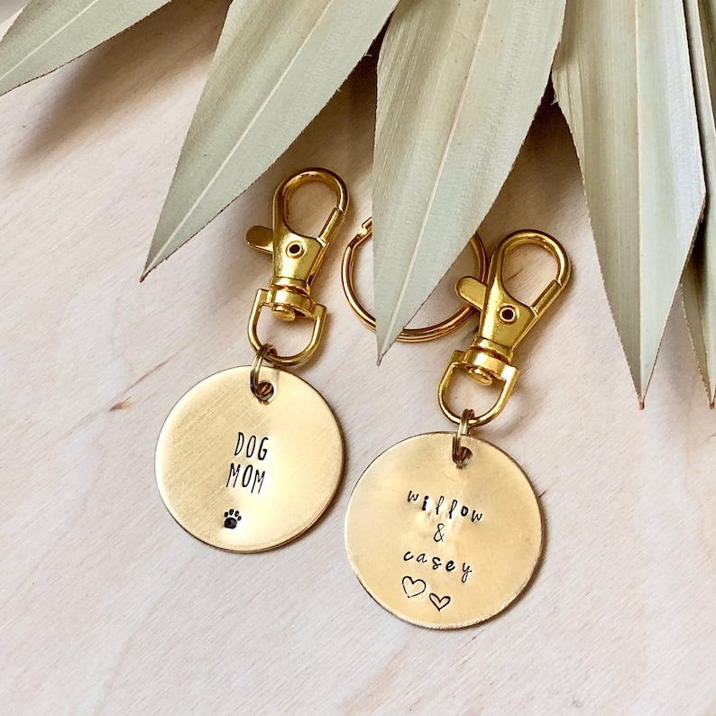 May include: Two gold keychains with round metal tags. One tag says "Dog Mom" with a paw print. The other tag says "Willow & Casey" with two hearts.
