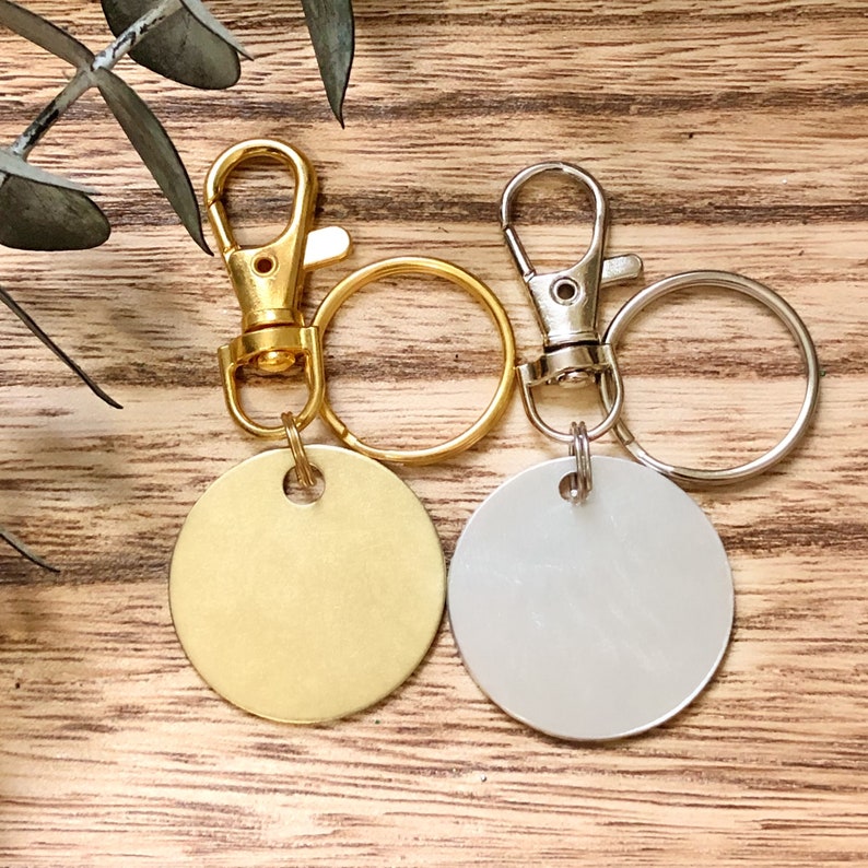 May include: Two keychains with round metal tags. One keychain has a gold tag and the other has a silver tag. Both keychains have a silver swivel clasp and a silver key ring.