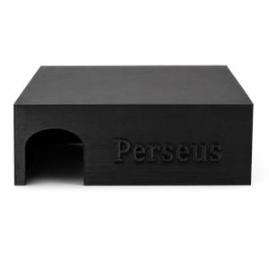 May include: A matte black rectangular pet hideout featuring a smooth top surface and a single arched entrance on the left side. The front panel displays the word Perseus in raised, embossed lettering, matching the dark finish of the structure.