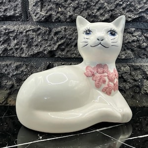 Vintage porseleinen kattenbloempot/wattenbolhouder, gemaakt in de jaren 1960-1970. Wit met handgeschilderd gezichtje en roze bloemenpatroon. Een ideaal cadeau voor kattenliefhebbers.