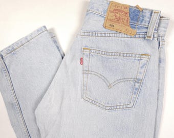 May include: Light blue denim jeans with a classic five-pocket design. The jeans feature a red Levi's tag on the back pocket and a brown leather label. The jeans are a light wash and appear to be vintage.
