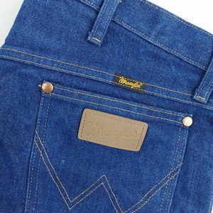 May include: A pair of blue denim jeans with a brown leather patch that says "Wrangler" on it. The jeans have a classic five-pocket style and a straight leg.
