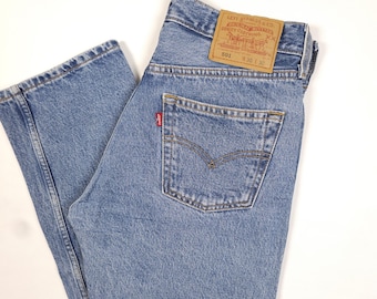May include: Light blue denim jeans with a classic five-pocket design. The jeans feature a red Levi's tag on the back pocket and a brown leather patch with the Levi Strauss & Co. logo. The waist size is 91 cm and the inseam is 76 cm.