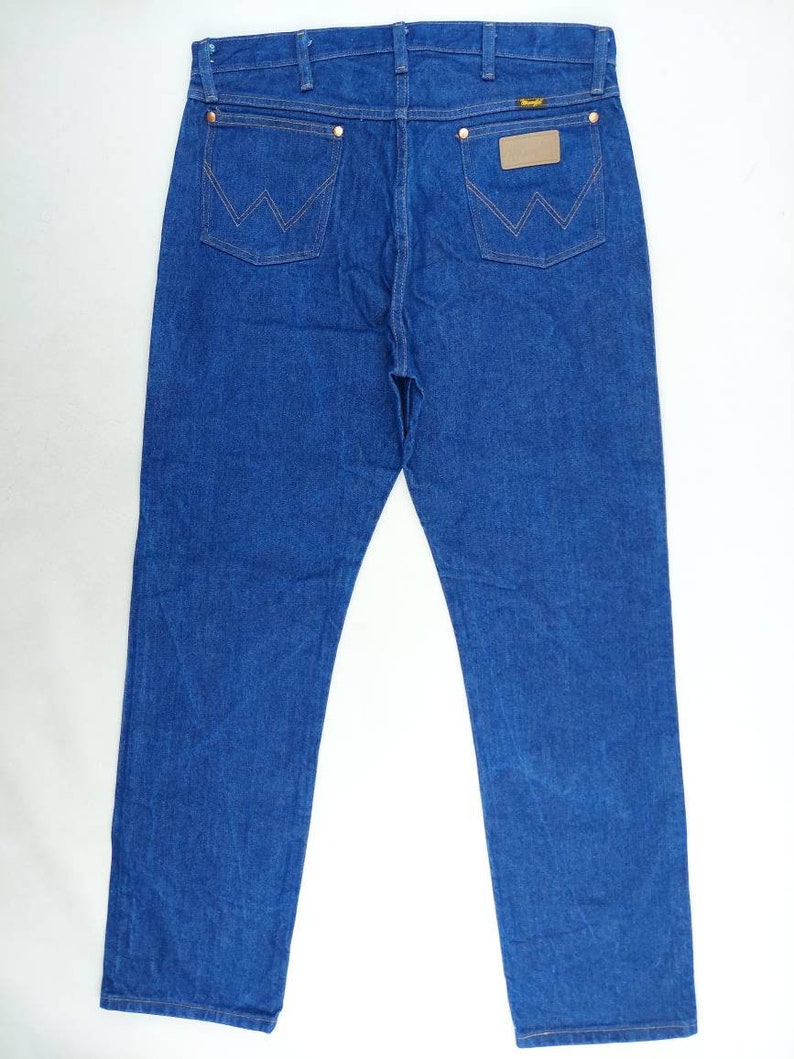 May include: A pair of blue denim jeans with a brown leather patch on the back pocket that says "Wrangler".