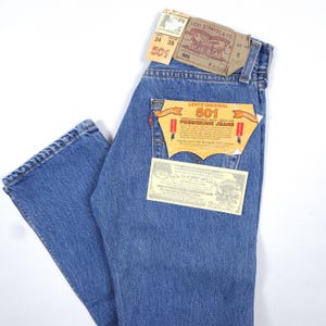 May include: Light blue Levi's 501 jeans with original tags attached. The tags include the Levi Strauss & Co. logo, size information, and the 501 model number. The jeans have a classic five-pocket design and a red Levi's tag on the back pocket.