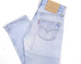 Puede incluir: Vaqueros de mezclilla azul claro con un diseño clásico de cinco bolsillos. Los vaqueros presentan un lavado descolorido y una pequeña etiqueta roja en el bolsillo trasero. Un parche de cuero marrón es visible en la cintura.