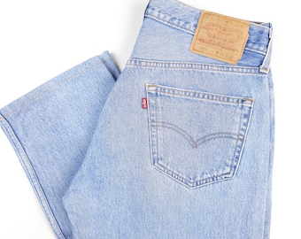 May include: Light blue denim jeans with a back pocket and a red Levi's label. The jeans have a brown leather patch with the Levi's logo and the text "ORIGINAL  RIVEted  CLOTHING  QUALITY  CLOTHING  501  XX  MADE IN THE USA".