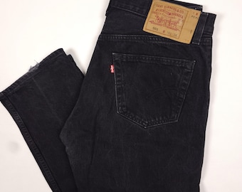 Könnte beinhalten: Schwarze Levi's 501 Jeans mit klassischem Fünf-Taschen-Design. Die Jeans haben ein rotes Levi's-Etikett auf der Gesäßtasche und einen braunen Lederaufnäher mit dem Levi Strauss & Co. Logo. Größe 34, aus strapazierfähigem Denim.