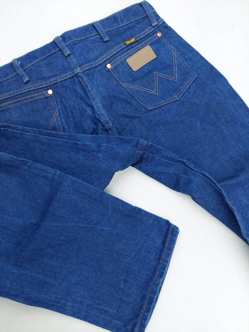 May include: A pair of blue denim jeans with a brown leather patch on the back pocket that says "Wrangler".