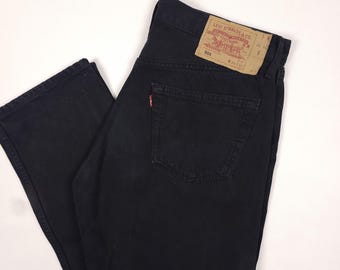 Könnte beinhalten: Schwarze Levi's 501 Jeans. Die Jeans haben ein klassisches Fünf-Taschen-Design, ein rotes Levi's-Etikett auf der Gesäßtasche und ein braunes Etikett mit dem Levi Strauss & Co. Logo. Die Jeans bestehen aus strapazierfähigem Denim-Material.