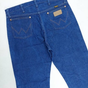 May include: A pair of blue denim jeans with a brown leather patch on the back pocket that says "Wrangler".