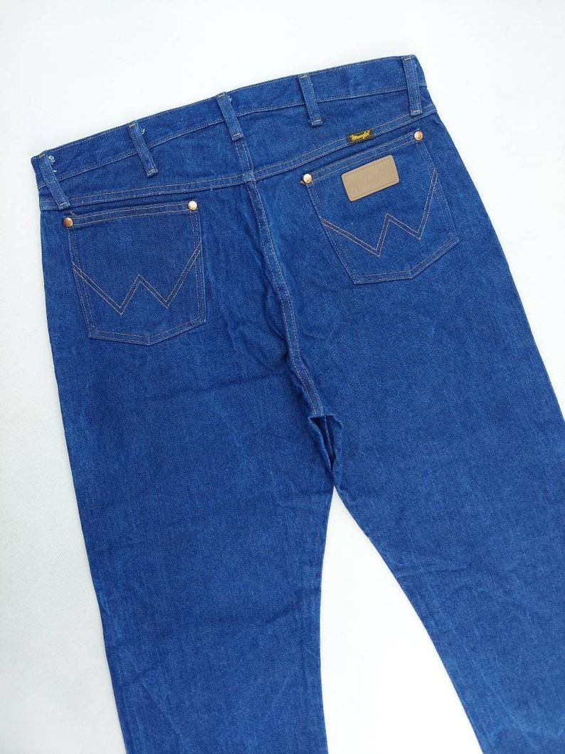 May include: A pair of blue denim jeans with a brown leather patch on the back pocket that says "Wrangler".