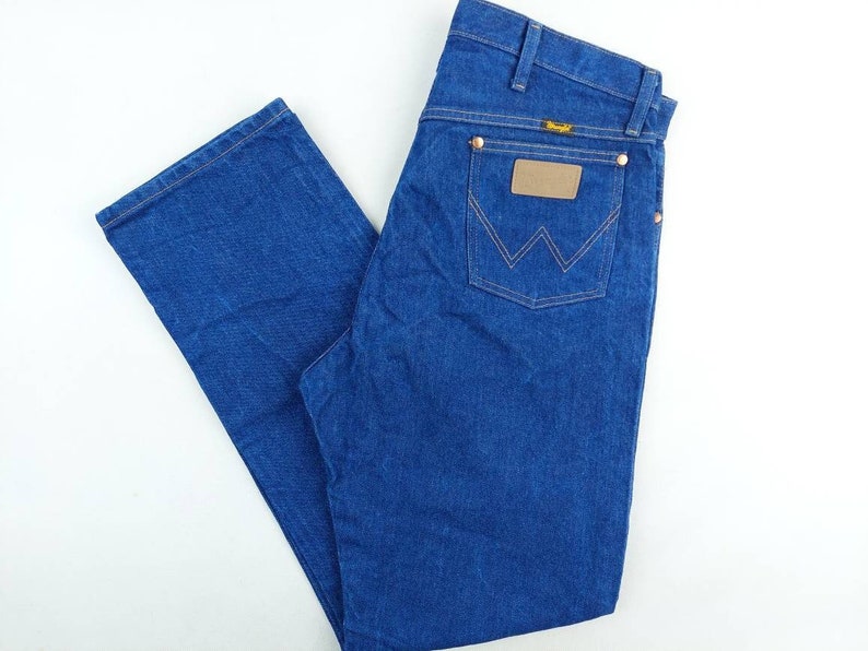 May include: A pair of blue denim jeans with a brown leather patch on the back pocket that says "Wrangler".