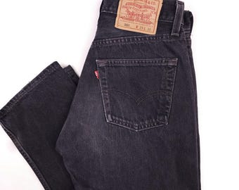 Peut inclure: Jean Levi's 501 gris foncé avec une conception classique à cinq poches. Le jean comporte une étiquette rouge Levi's sur la poche arrière et un patch en cuir marron avec le logo Levi's. Taille W29, longueur 76 cm.