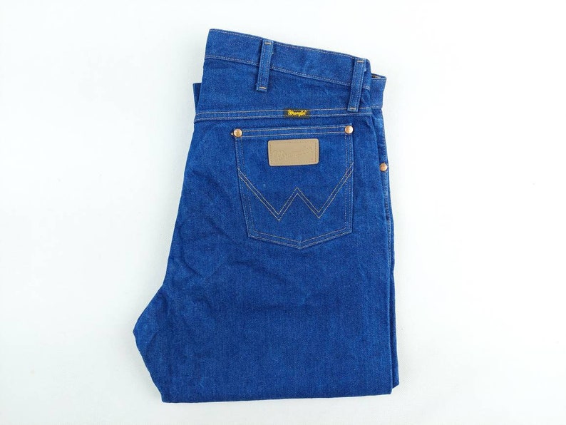 May include: A pair of blue denim jeans with a brown leather patch on the back pocket that says "Wrangler".
