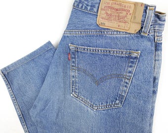 May include: A pair of blue denim jeans with a brown leather patch on the back pocket. The patch has the text "Levi Strauss & Co.  Original  Quality Clothing  XX  501  W 31 L 32".