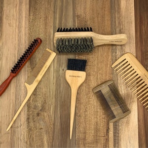 Könnte beinhalten: Ein Set aus sechs Holzbürsten und Kämmen für Haare, darunter eine Wildschweinborstenbürste, ein Kamm mit langem Griff und ein kleiner Kamm. Die Bürsten und Kämme sind alle aus Naturholz gefertigt und haben eine hellbraune Farbe.