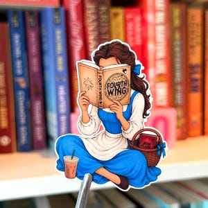 May include: A die-cut sticker featuring a brown-haired character in a blue dress and white apron reading a book titled Fourth Wing. The character sits with a wicker basket containing a book titled Iron Flame and an iced coffee with a green straw.