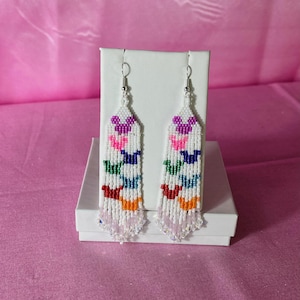 May include: A pair of long, white beaded earrings with a colorful butterfly design. The earrings have a crystal fringe at the bottom.