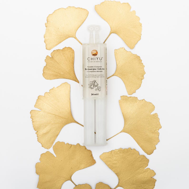 May include: A clear, two-part glue tube with the text "CHIYU" and "Bio-based glue" is centered on a white background. The glue tube is surrounded by golden-colored ginkgo leaves. The tube contains 24 ml of glue.