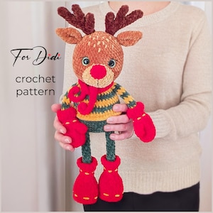 Op de afbeelding: Een handgemaakte gehaakte rendierpop met een rode neus, sjaal, wanten en laarzen. Het rendier heeft bruine geweien, een gestreepte geel-groene trui en de tekst "For Didi crochet pattern".