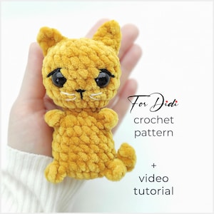 Puede incluir: Un gato de ganchillo amarillo hecho a mano, con ojos negros y un bigote blanco. El gato está en la mano de una persona. El texto "For Didi crochet pattern + video tutorial" es visible.