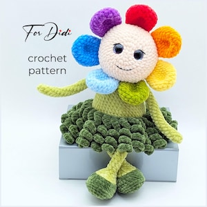 May include: A handmade crochet flower doll with a smiling face, rainbow petals, and a green skirt. The doll has long arms and legs, and the text "For Didi" and "crochet pattern" are visible.