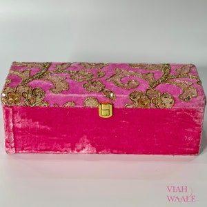 May include: A pink velvet jewellery box with a gold clasp and a floral design on the lid.