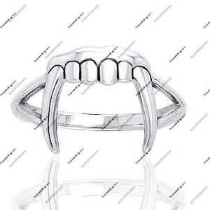 May include: A silver-colored ring featuring a stylized vampire teeth design. The ring has a band and a prominent set of fangs and teeth, creating a bold and unique accessory. The ring is shown against a white background.