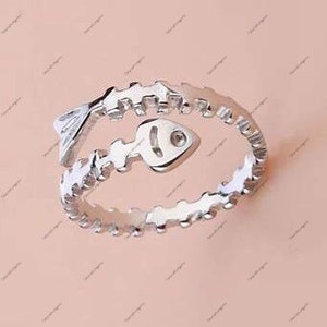 Puede incluir: Un anillo de plata con un diseño de espina de pescado. El anillo está abierto y tiene un diseño de espina de pescado con una cabeza de pez al final.