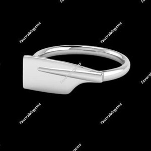 May include: A silver ring with a stylized oar design. The ring is a simple band with a flat, wide oar shape on the top.