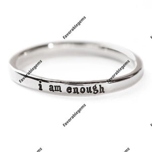 May include: A silver ring with the words "i am enough" engraved on the band.