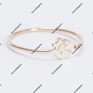 May include: A gold-colored ring featuring a Pac-Man design. The ring has a thin band and an open design, with the Pac-Man figure on the front. The ring is likely made of gold or a gold-colored metal.