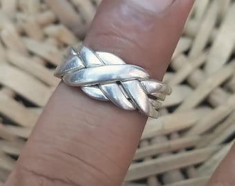 Könnte beinhalten: Ein silberner Ring mit einem mehrbändigen Design aus ineinandergreifenden Strängen, die ein geflochtenes oder gewebtes Aussehen erzeugen. Das Metall hat eine polierte, reflektierende Oberfläche mit glatten, abgerundeten Kanten.