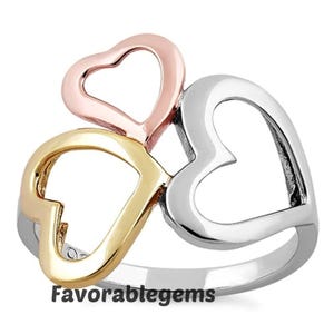 May include: A ring featuring three heart-shaped designs in rose gold, gold, and silver, set on a silver band. The ring has the text "Favorablegems" on the band.