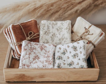 May include: A wooden tray holds stacks of square, patterned cloths tied with twine. The cloths feature floral designs in shades of brown, cream, and blue. Some cloths are solid brown with white trim.