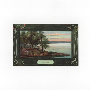 May include: A rectangular framed print featuring a landscape of a lake at sunset with pine trees along the shore. The dark green frame has a wood grain texture, thin light green decorative lines, small red dots, and a label reading SOLITUDE.